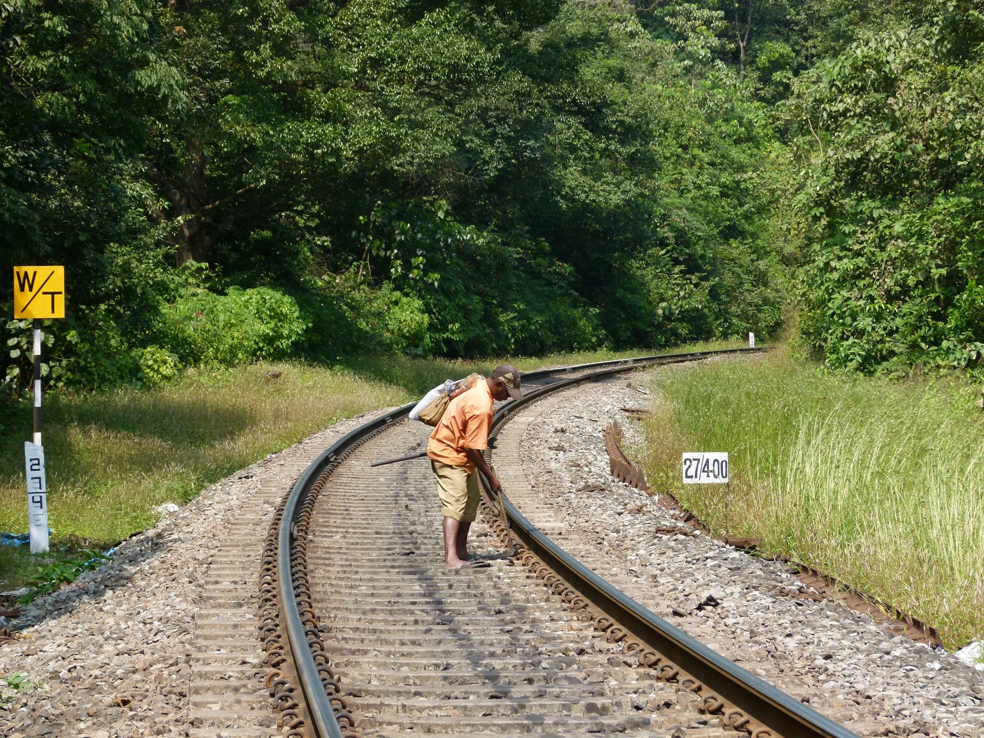 Trabalhador a percorrer a via a pé e a apertar as fixações do carril